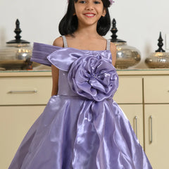 Young girl wearing a purple dress with a large flower detail in a room.