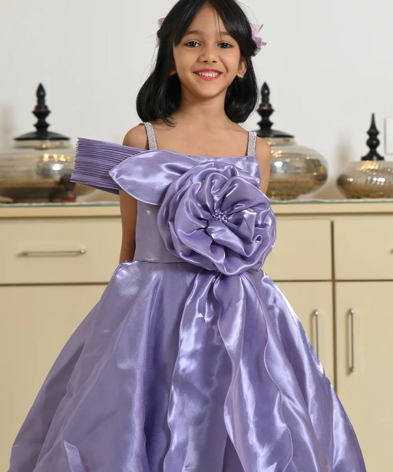 Young girl wearing a purple dress with a large flower detail in a room.