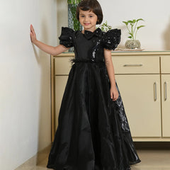 Young girl in a black dress standing indoors with a neutral background