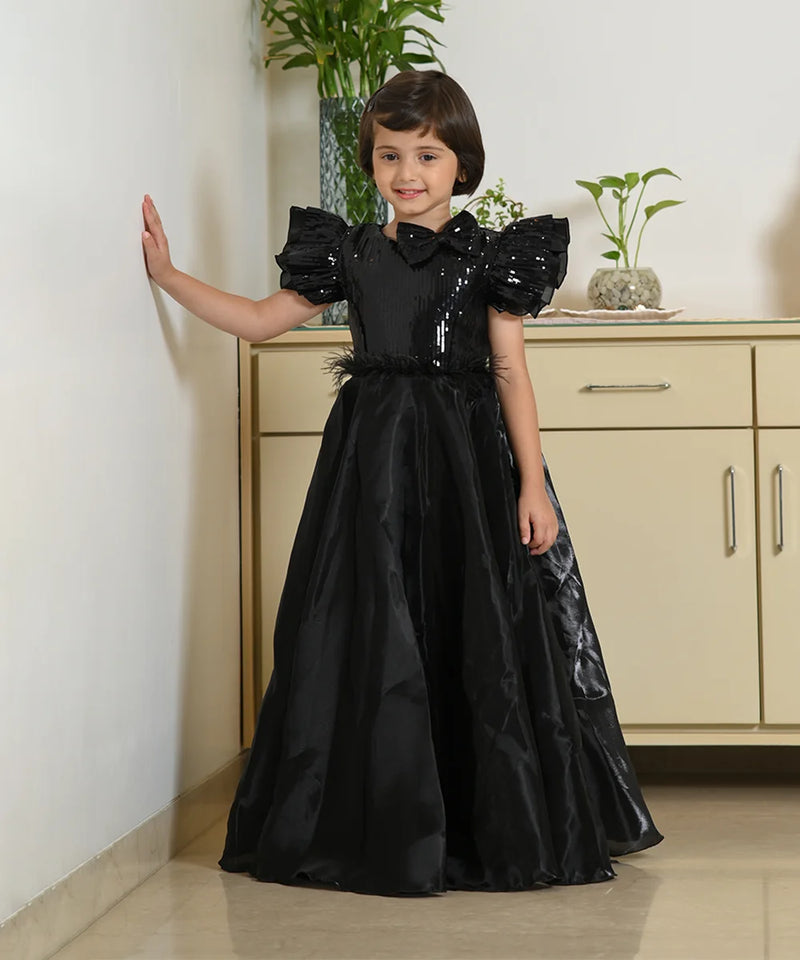 Young girl in a black dress standing indoors with a neutral background