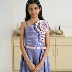 Young girl in a lavender dress with a large floral embellishment in a room.