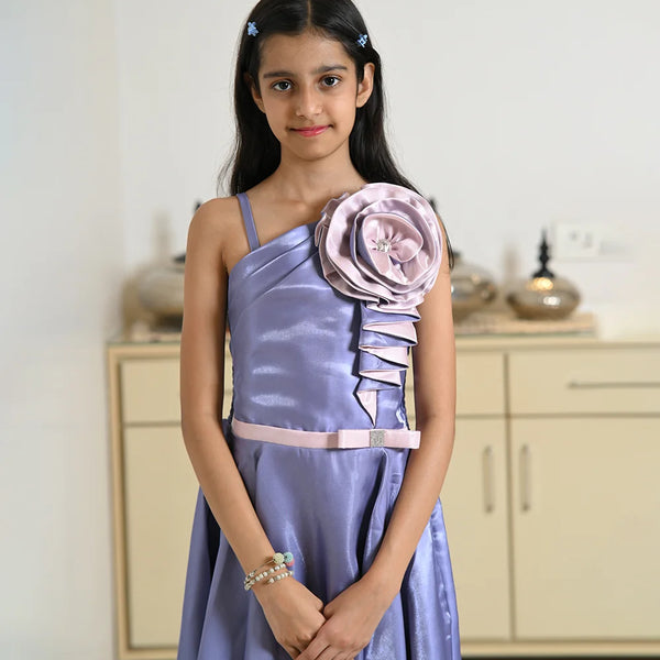 Young girl in a lavender dress with a large floral embellishment in a room.