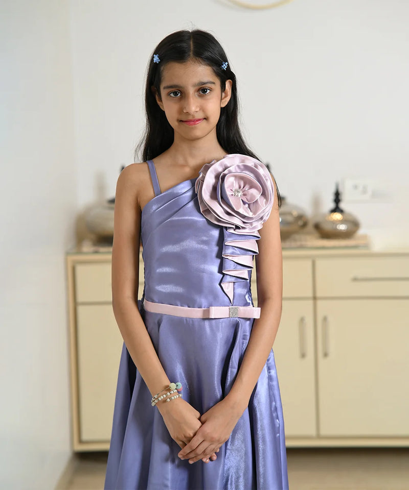 Young girl in a lavender dress with a large floral embellishment in a room.