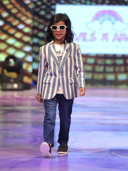 Child Model walking on a runway wearing a striped blazer and sunglasses with a colorful background.
