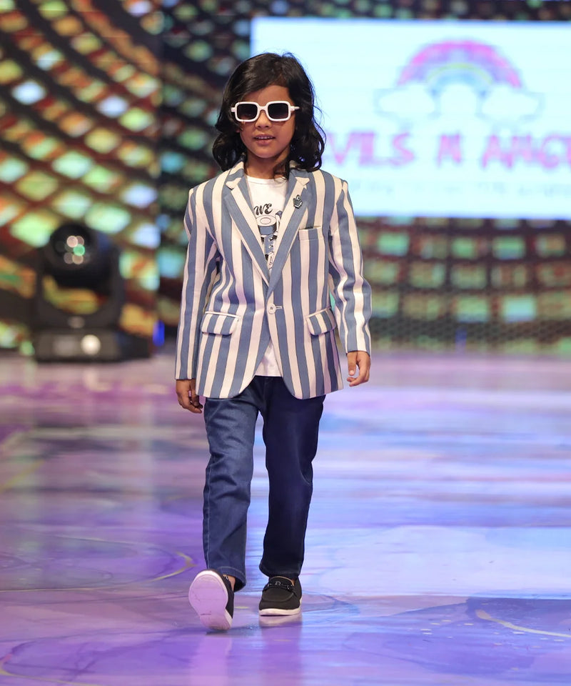 Child Model walking on a runway wearing a striped blazer and sunglasses with a colorful background.