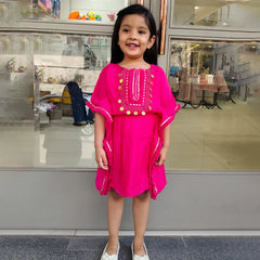 Young girl in a bright pink dress standing in front of a store window.