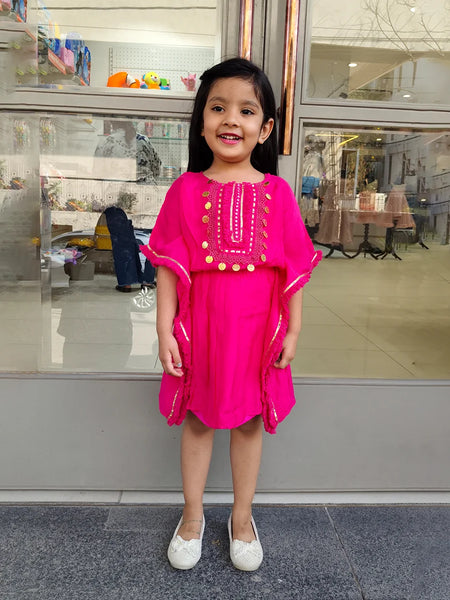 Young girl in a bright pink dress standing in front of a store window.