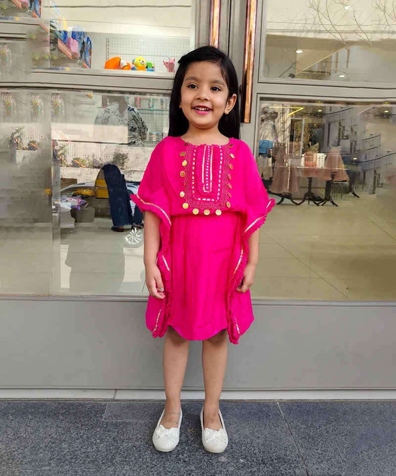 Young girl in a bright pink dress standing in front of a store window.