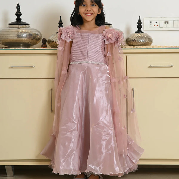 Young girl in a pink dress standing in front of a beige cabinet.