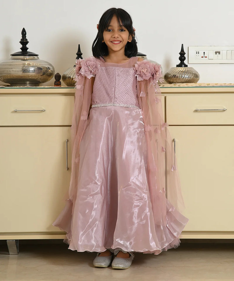 Young girl in a pink dress standing in front of a beige cabinet.