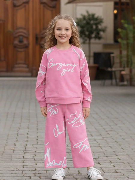 Young girl wearing a pink outfit with text, standing on a stone pavement.