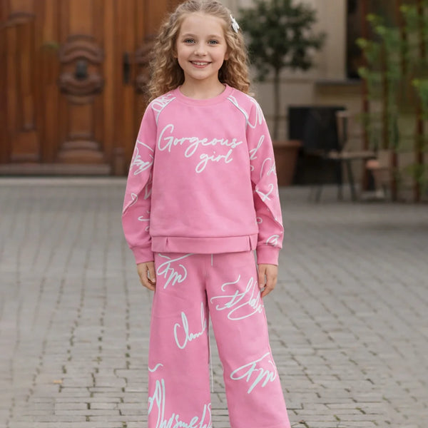 Young girl wearing a pink outfit with text, standing on a stone pavement.