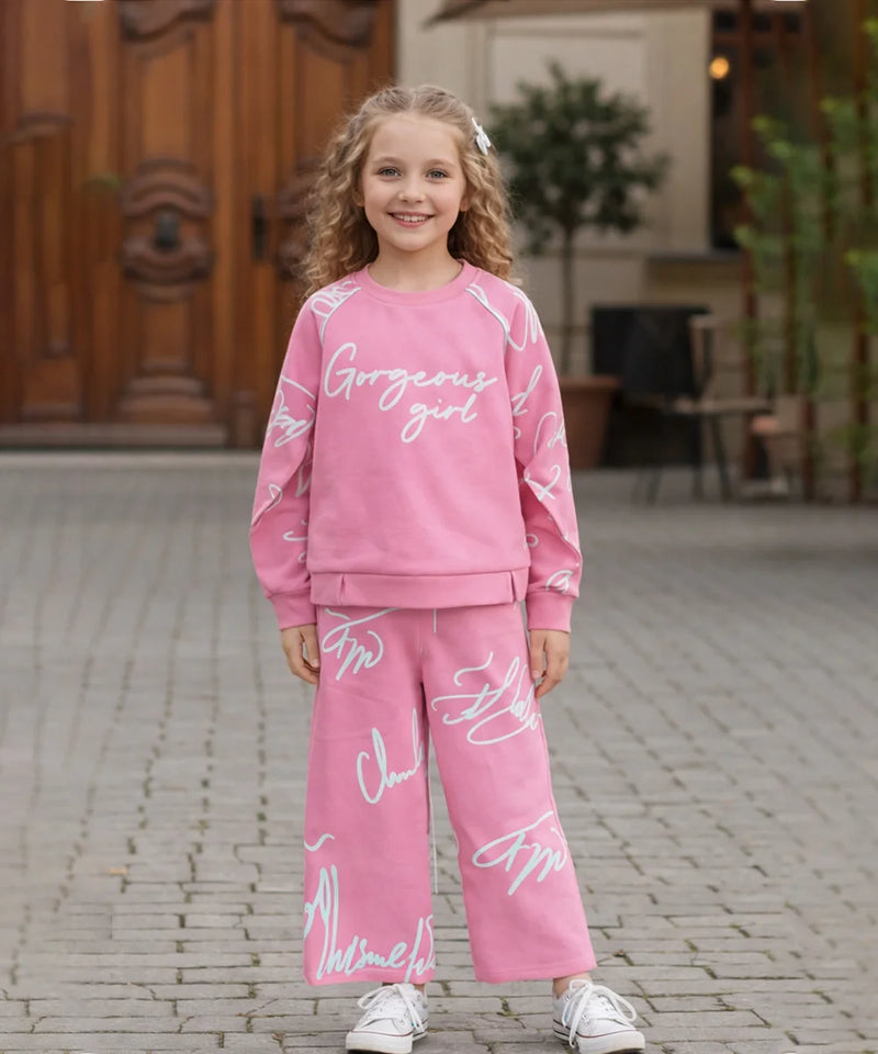 Young girl wearing a pink outfit with text, standing on a stone pavement.