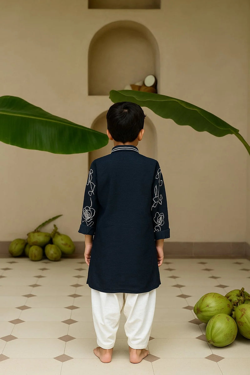 Child wearing a dark blue kurta with white embroidery in a room with green fruits and leaves.