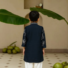 Child wearing a dark blue kurta with white embroidery in a room with green fruits and leaves.