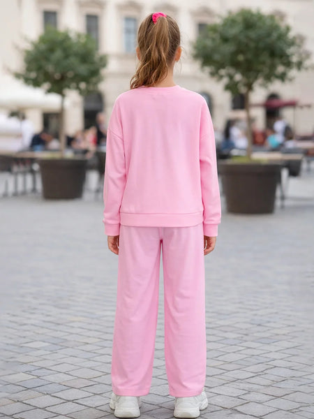 Person wearing a pink tracksuit standing on a paved area with trees and people in the background.
