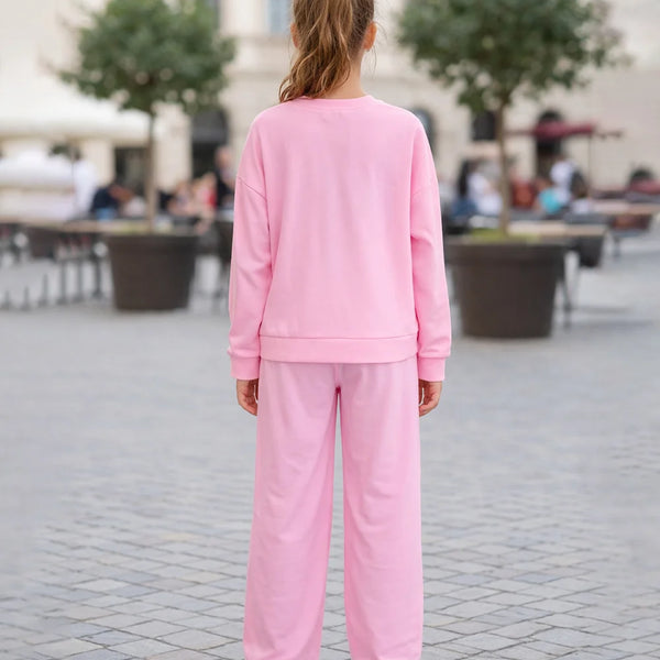 Person wearing a pink tracksuit standing on a paved area with trees and people in the background.