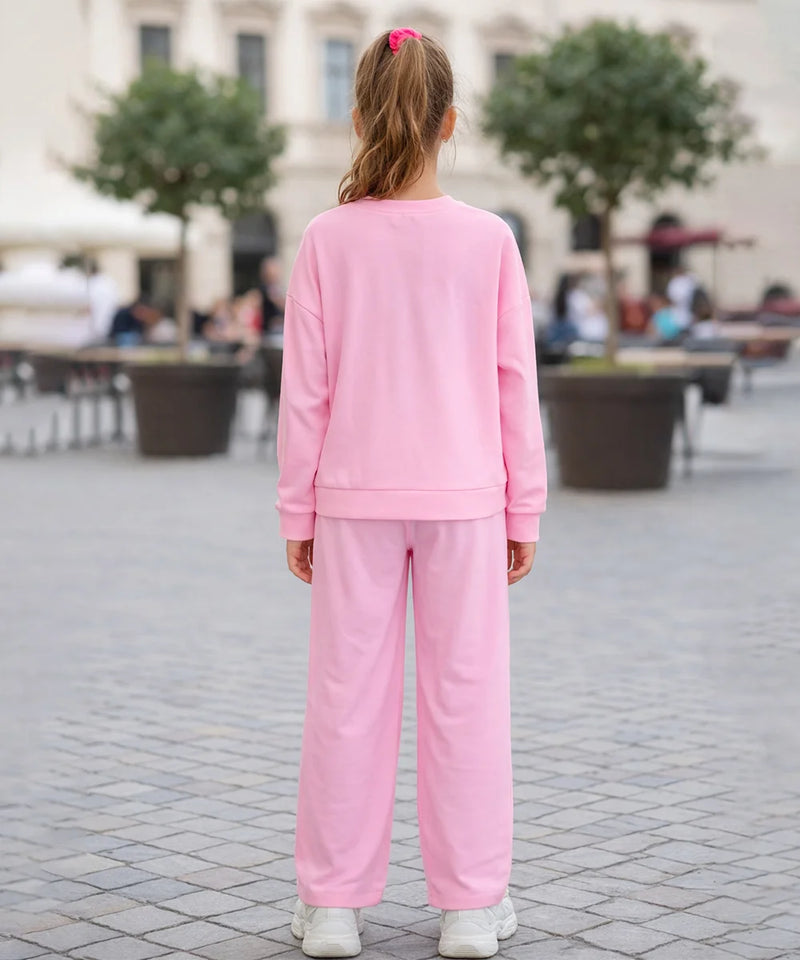 Person wearing a pink tracksuit standing on a paved area with trees and people in the background.