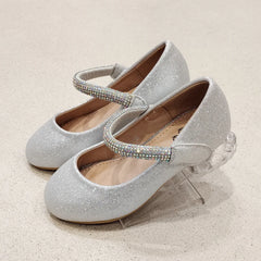 Silver glittery shoes with rhinestone straps on a light beige background