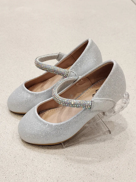 Silver glittery shoes with rhinestone straps on a light beige background