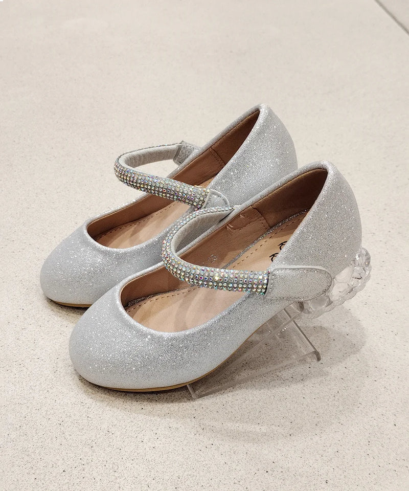 Silver glittery shoes with rhinestone straps on a light beige background