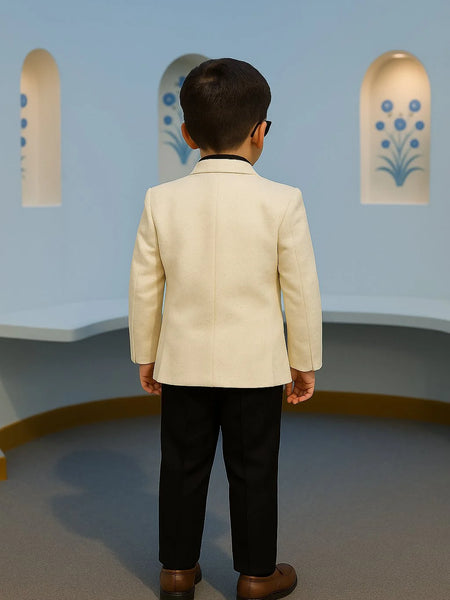 Child wearing a beige blazer and black pants standing in front of a light blue wall with decorative elements.