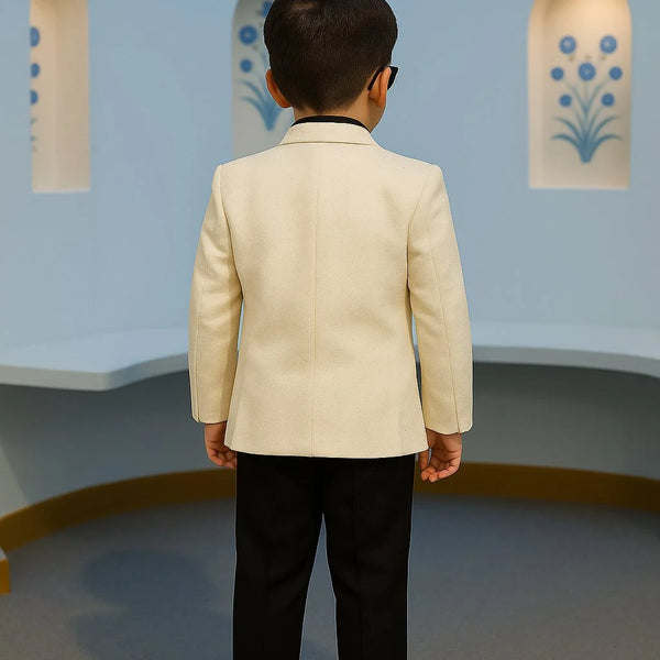 Child wearing a beige blazer and black pants standing in front of a light blue wall with decorative elements.