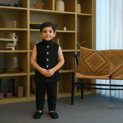 Child in a formal outfit standing in a room with a bookshelf and chair.