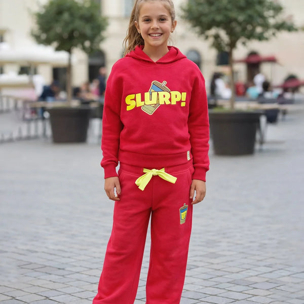 Child wearing a red 'SLURP!' hoodie and pants in an outdoor setting