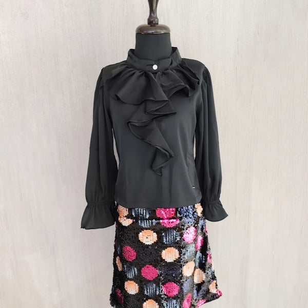Black ruffled blouse with a colorful polka dot skirt on a mannequin against a plain background