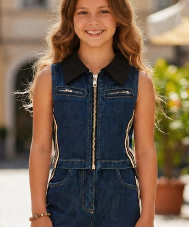 Young girl wearing a denim jumpsuit with a black collar in an outdoor setting.