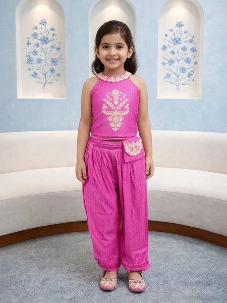 Young girl in a pink traditional outfit standing in a room with decorative elements.