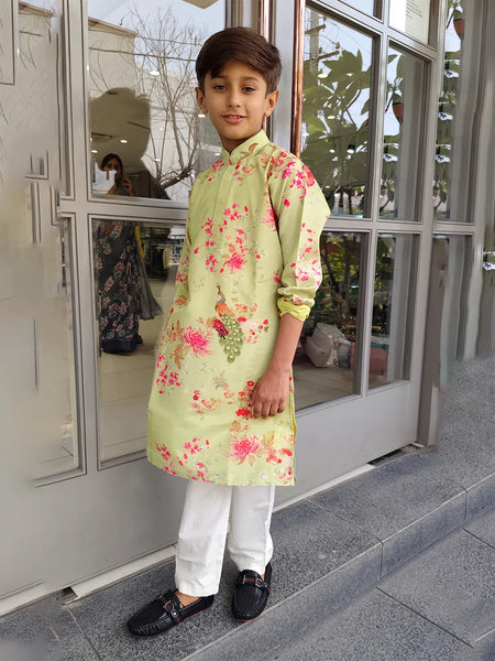 Child wearing a light green kurta with floral patterns standing outside a building.