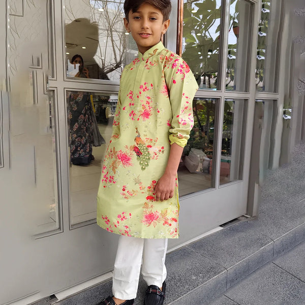 Child wearing a light green kurta with floral patterns standing outside a building.