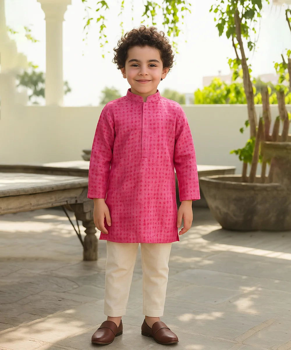 Child wearing a bright pink kurta with white pants outdoors.