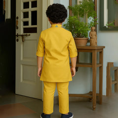 Child in a yellow outfit standing in a room with a door and wooden table.