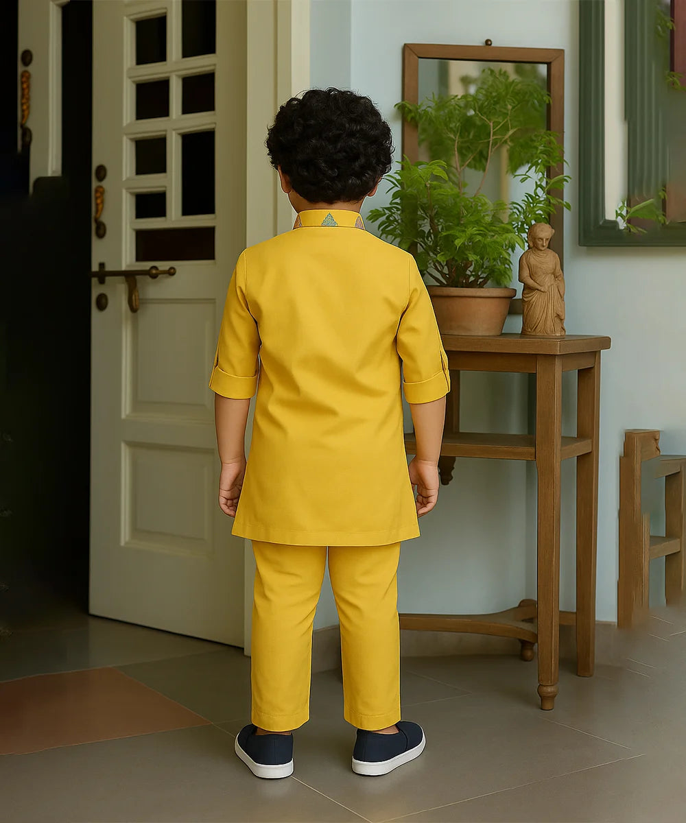 Child in a yellow outfit standing in a room with a door and wooden table.