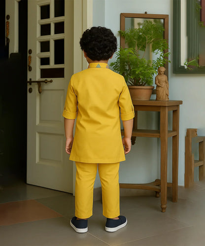 Child in a yellow outfit standing in a room with a door and wooden table.