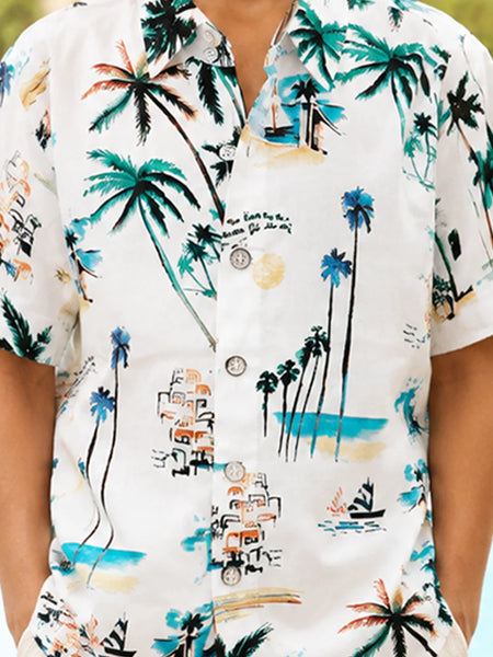 A man wearing a white short-sleeve button-up shirt with a colorful tropical beach print featuring palm trees, boats, and buildings.