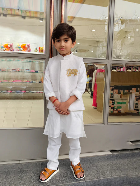 Young boy in a white traditional outfit standing in front of a store display.