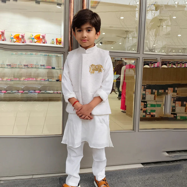 Young boy in a white traditional outfit standing in front of a store display.