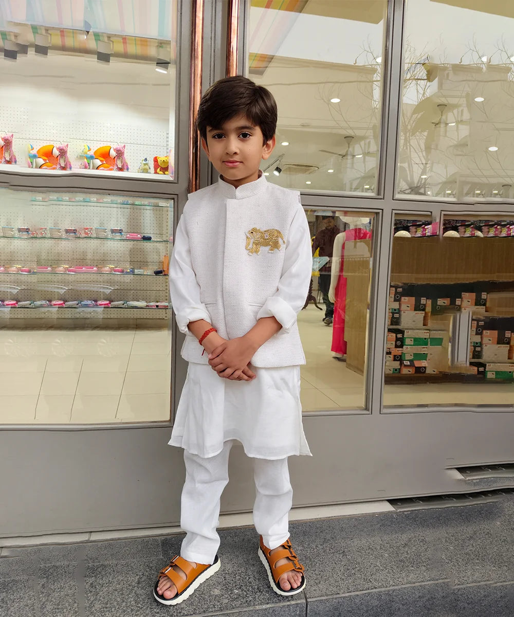 Young boy in a white traditional outfit standing in front of a store display.