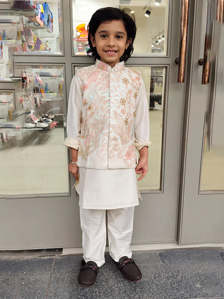 Child wearing a kurta pyjama with a jacket traditional outfit standing in front of a store entrance.