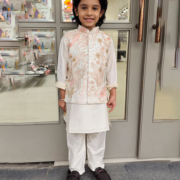 Child wearing a kurta pyjama with a jacket traditional outfit standing in front of a store entrance.