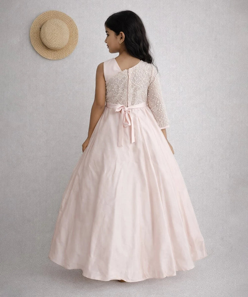 Woman wearing a long dress with a lace top and pink skirt, standing against a plain background.