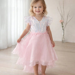 Young girl wearing a pink dress with ruffled sleeves in a softly lit room.