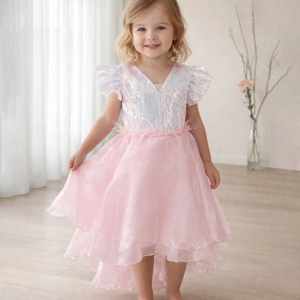 Young girl wearing a pink dress with ruffled sleeves in a softly lit room.