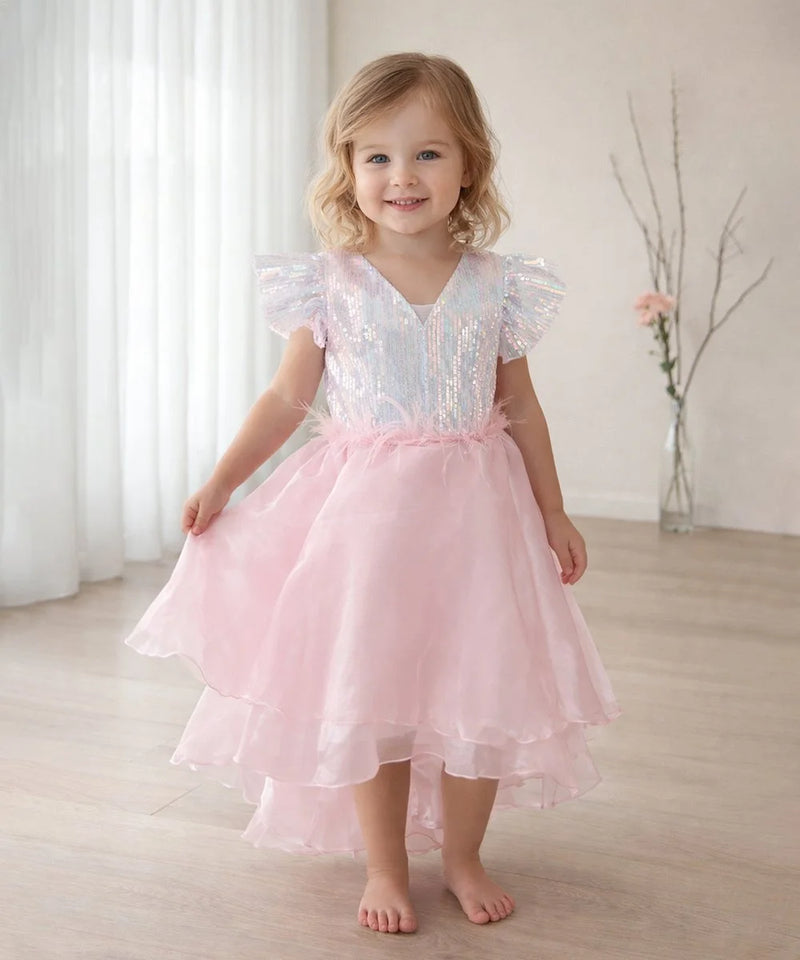 Young girl wearing a pink dress with ruffled sleeves in a softly lit room.