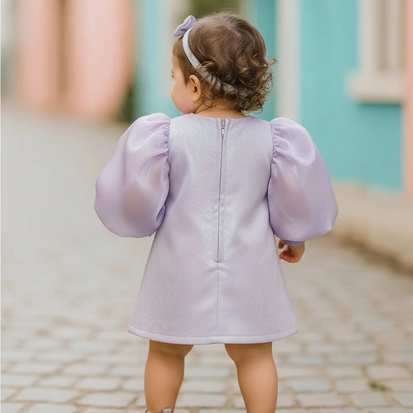 Child wearing a light purple dress with puffed sleeves on a cobblestone street.