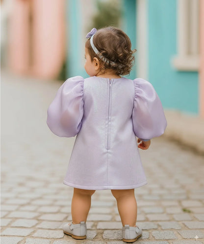 Child wearing a light purple dress with puffed sleeves on a cobblestone street.